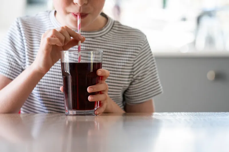 close up of girl drinking sugary fizzy soda from glass with straw