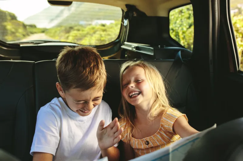 small boy and girl sitting on backseat of car looking at map and smiling kids traveling in a car on roadtrip playing with a map