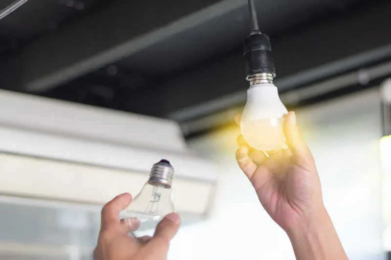 power saving concept asia man changing compact-fluorescent (cfl) bulbs with new led light bulb
