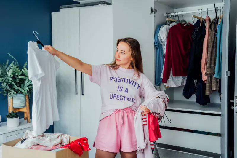woman selecting clothes from her wardrobe for donating to a charity shop decluttering, sorting clothes and cleaning up reuse, second-hand concept conscious consumer, sustainable lifestyle