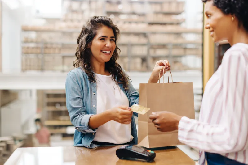 happy female customer paying her bill with a credit card in a ceramic store cheerful young woman smiling happily while shopping from a local female-owned small business