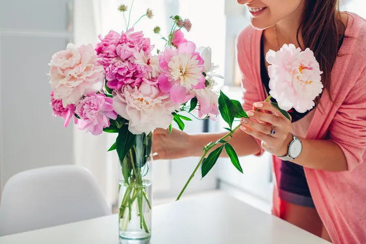 woman puts pink peonies flowers in vase young housewife taking care of coziness on kitchen composing bouquet home decor