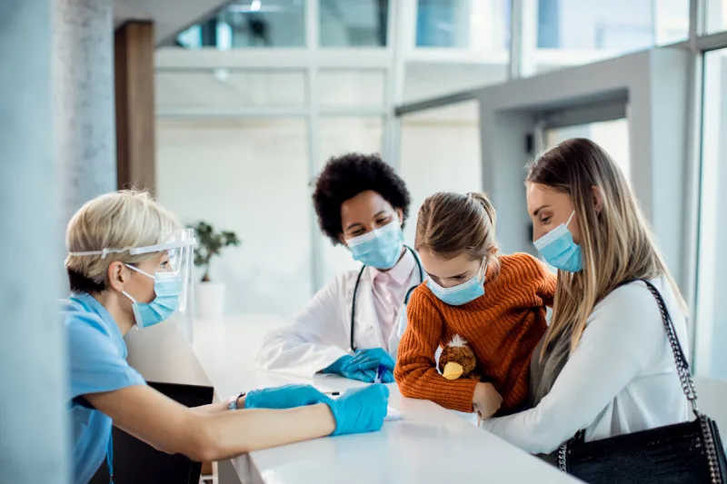 little girl and her mother talking to a nurse at reception desk in the hospital during covid-19 pandemic