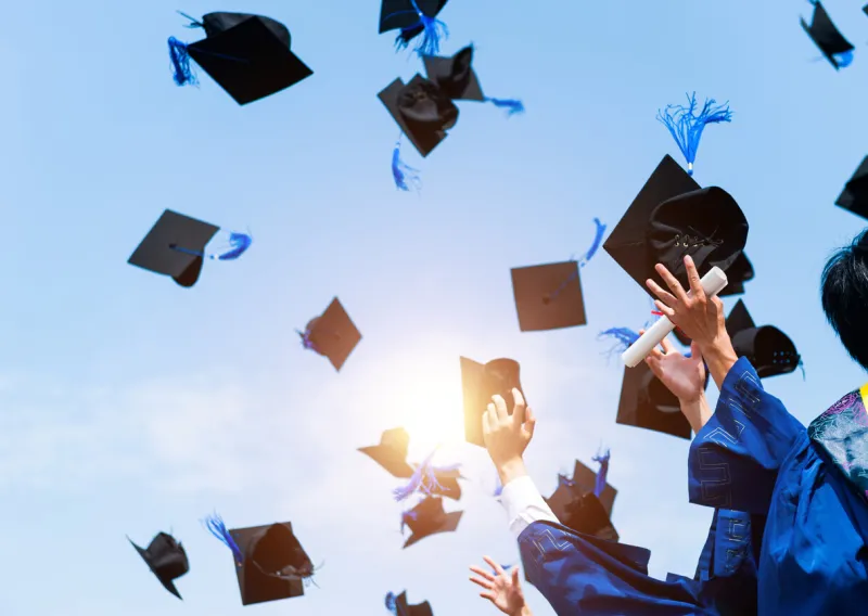 graduating students hands throwing graduation caps in the air