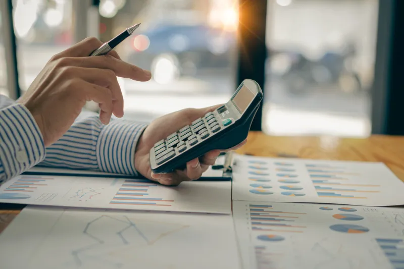 at the accounting desk, an accountant presses a calculator to analyze investment charts to generate monthly financial reports or company profits