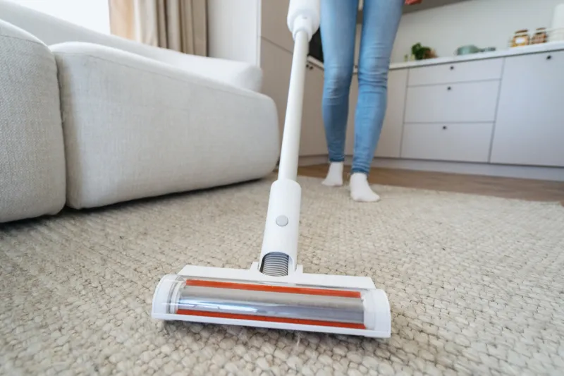 housework and housekeeping concept selective focus at brush on modern and cordless vacuum cleaner cropped woman using professional appliance to hoovering carpet at home