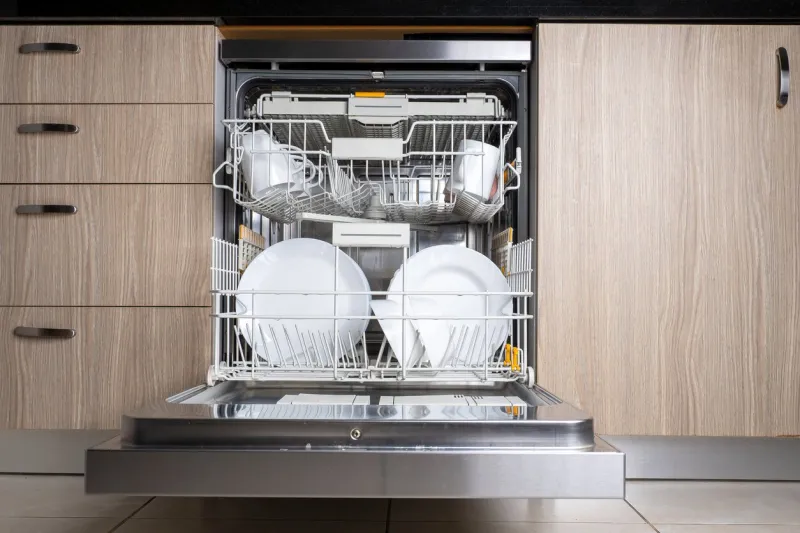 open door of built-in dishwasher kitchen with integrated appliances plates and dishes in the dishwasher