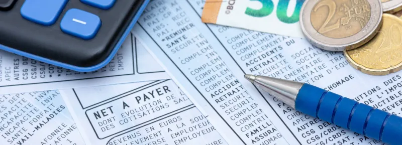 close up on a french payroll with social contributions and income tax deduction, mandatory in france since january 2019, along with euro cash, a pen and a calculator