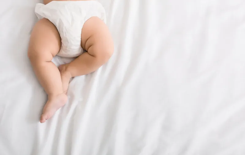 baby legs and bottom in diaper on white bed background, top view, copy space