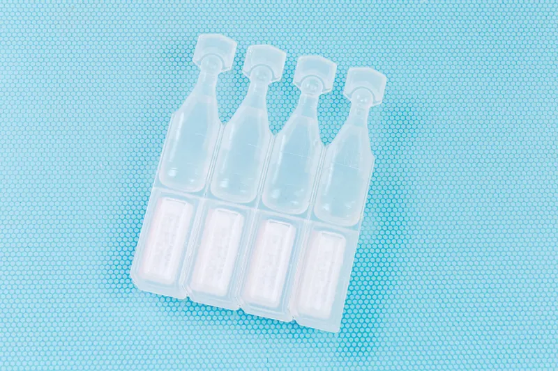 eye drops in small disposable plastic ampoules connected in block, top view close-up on a blue surface