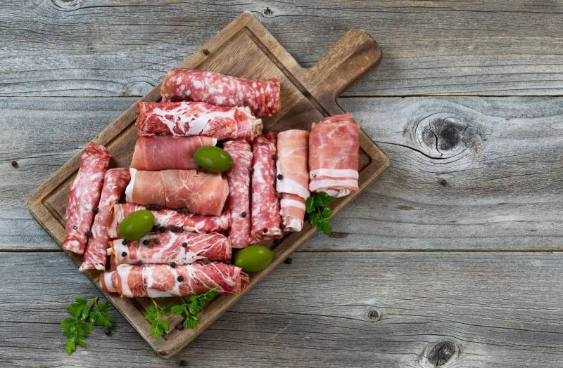 top view horizontal image of various meats on serving board with ham, pork, beef, parsley, and olives on rustic wood