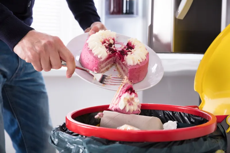 close-up of a human hand throwing cake in trash bin