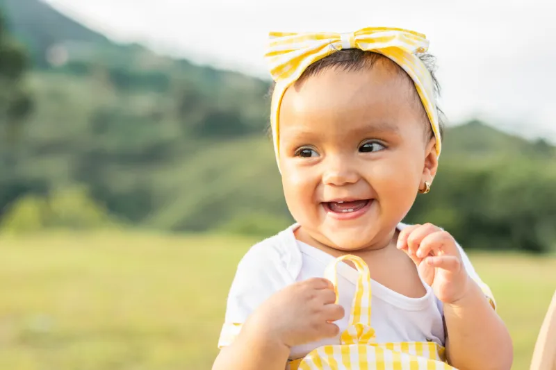 beautiful brown-skinned latina baby in an outdoor field on a summer day, smiling and showing her little teeth that are still coming out of her gums copy space