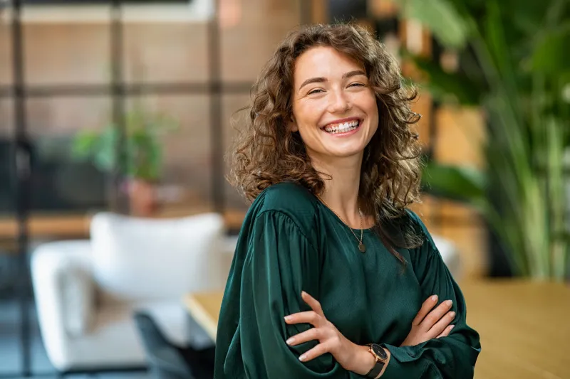 portrait of young smiling woman looking at camera with crossed arms happy girl standing in creative office successful businesswoman standing in office with copy space