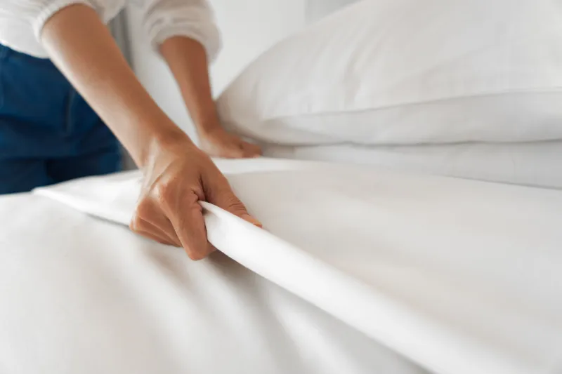 female hand set up white bed sheet in bedroom
