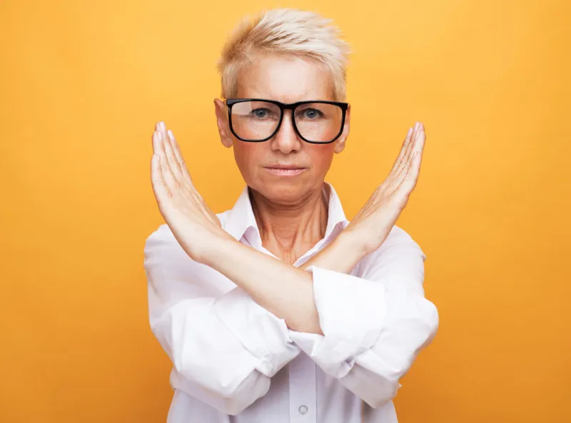 lifestyle, emotion and old people concept  senior woman with short gray hair wearing white shirt and glasses rejection expression crossing arms doing negative sign over yellow background