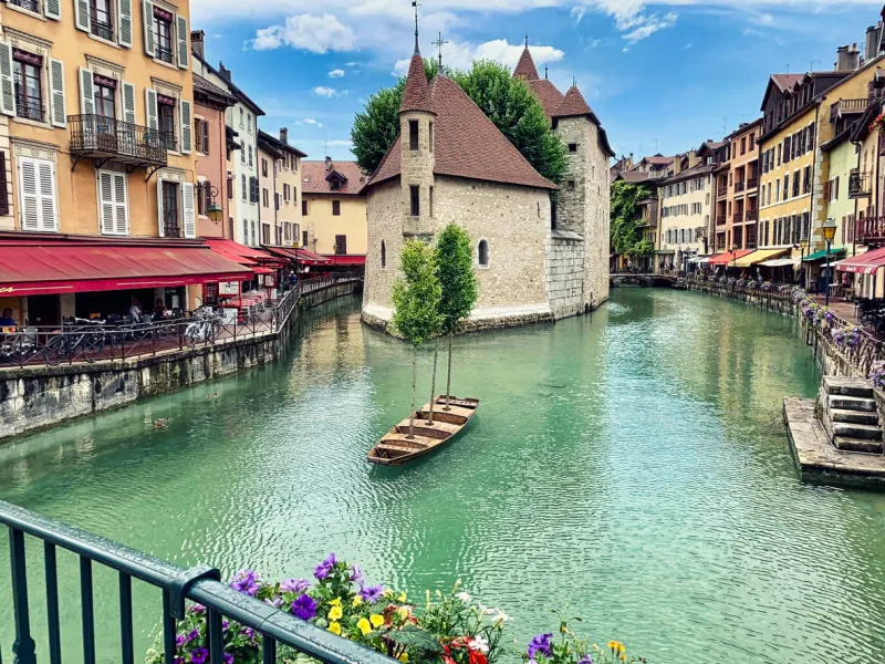 annecy, france - june 13, 2020 view of the historic district of annecy old town in the foreground, the river thiou on which a decorative boat is visible in the background, the picturesque old buildings of annecy