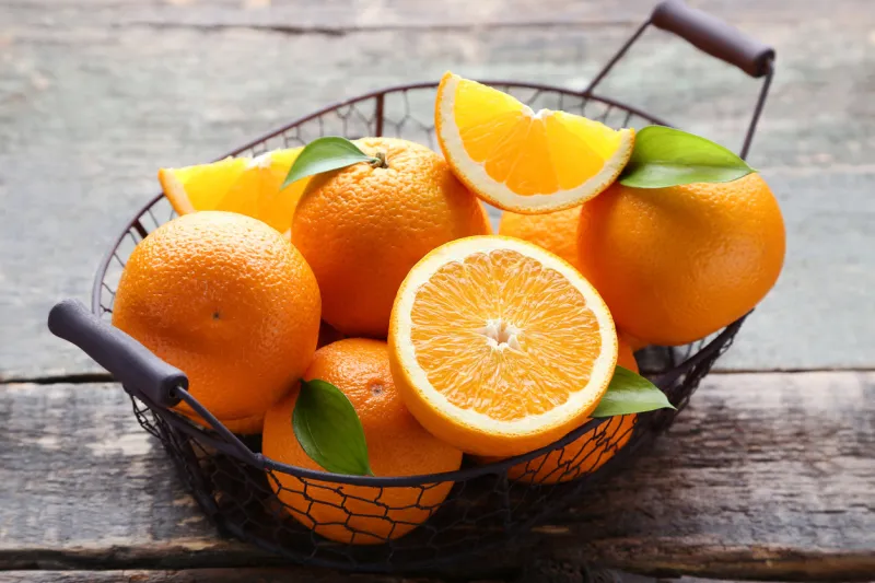 orange fruit with green leafs in basket on grey wooden table