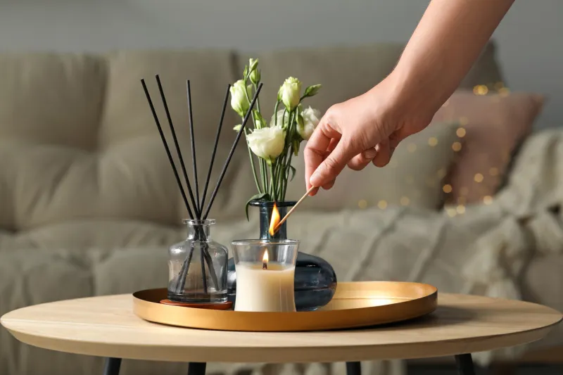 woman lighting candle at wooden table in living room, closeup