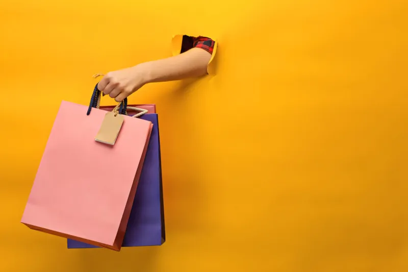 female hand holding bright shopping bags on yellow
