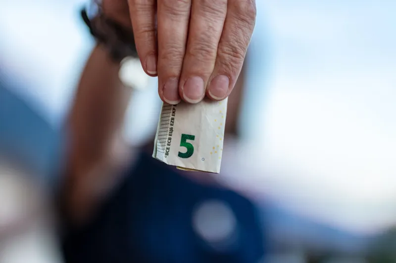 five euro in cash, focus on a folded european currency, held by four unrecognizable person's finger, shallow depth of field on the body in background