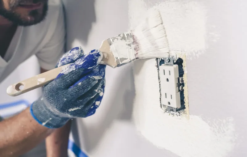 painter man with gloves painting the wall around power outlet