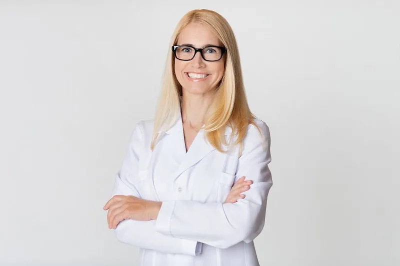friendly woman doctor in white uniform, smiling to camera on grey studio background
