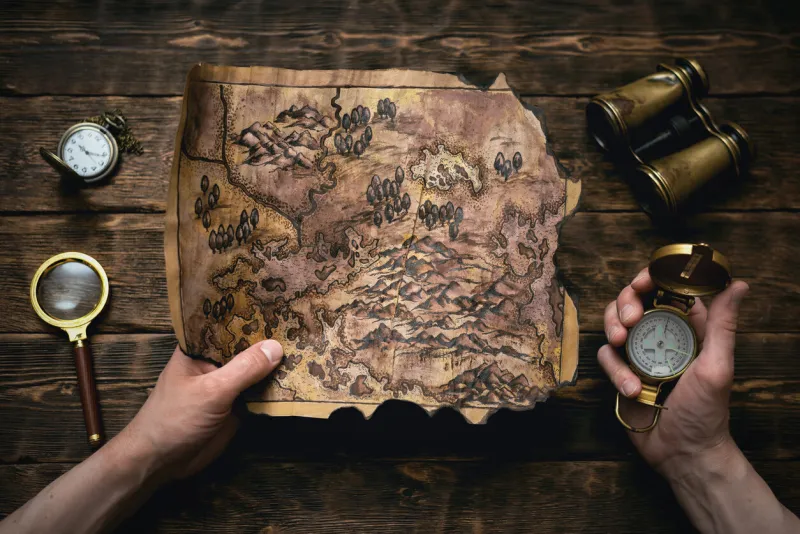 old map in man adventurer hands on a brown table background treasure hunt concept