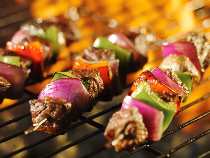 steak shishkabob skewers cooking on flaming barbecue grill
