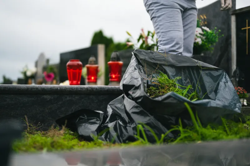 cemetery autumn cleaning before the all saints day unrecognizable person with a big black plastic bag full of collected grass from graveyard and red lanterns in background