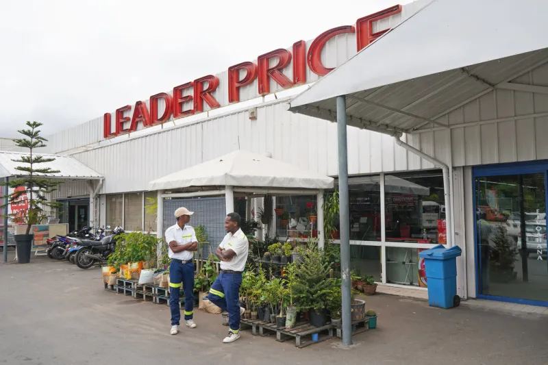 antananarivo, madagascar - april 24, 2019  two employees standing in front of leader price supermarket where plants are displayed this french discount store has branches in many african countries