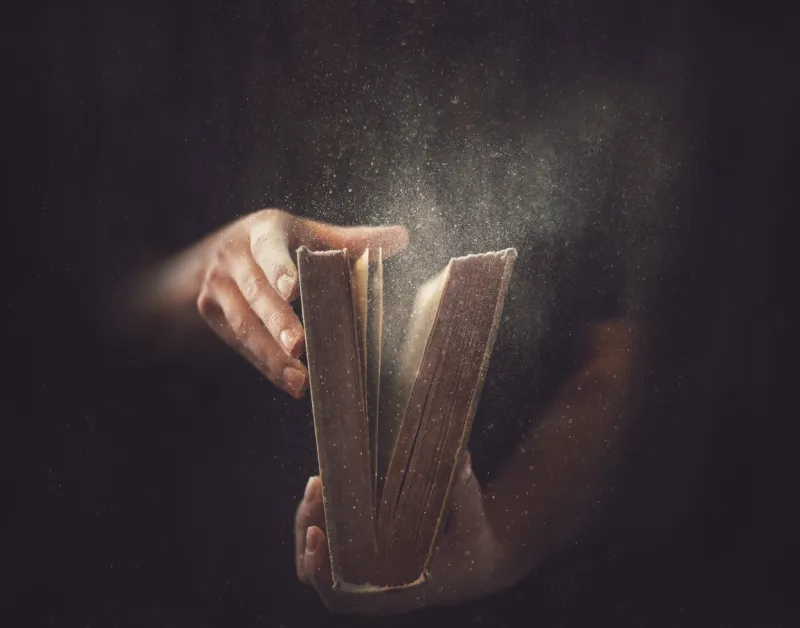 holding an open book with dust coming out