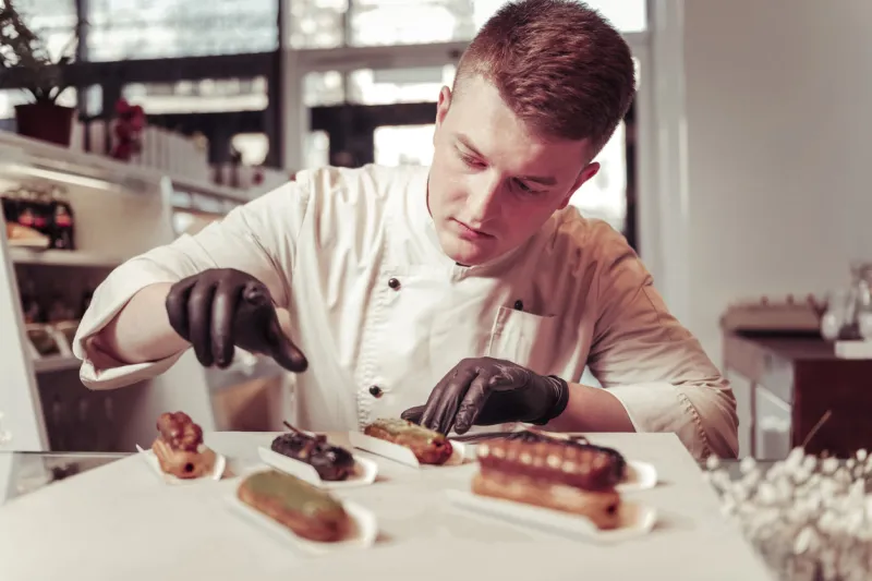 real professional serious skilled pastry chef focusing on his work while preparing eclairs