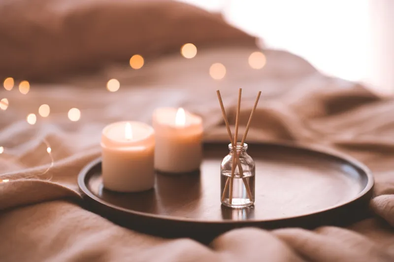 aroma bamboo sticks in bottle with scented liquid with candles staying on wooden tray in bed closeup