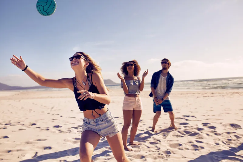 group of friends playing volleyball on the sandy beach and having fun young people on summer holidays playing with ball on the beach
