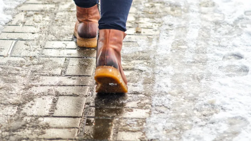 walk on wet melted ice pavement back view on the feet of a man walking along the icy pavement pair of shoe on icy road in winter abstract empty blank winter weather background