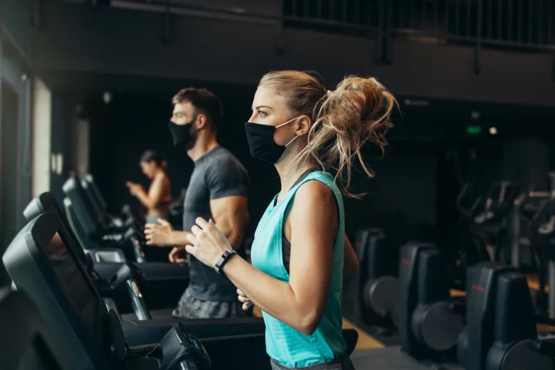 young fit woman and man running on treadmill in modern fitness gym they keeping distance and wearing protective face masks coronavirus world pandemic and sport theme