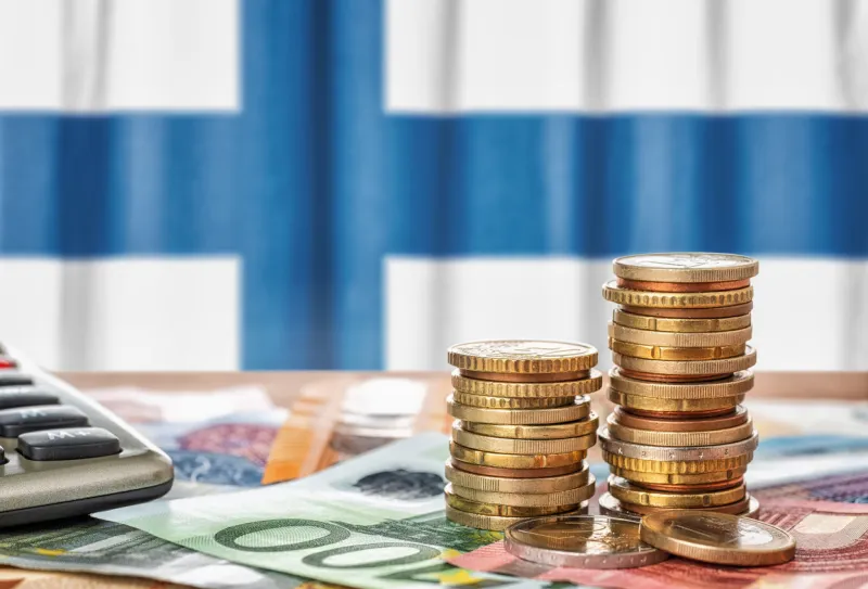 euro banknotes and coins in front of the national flag of finland