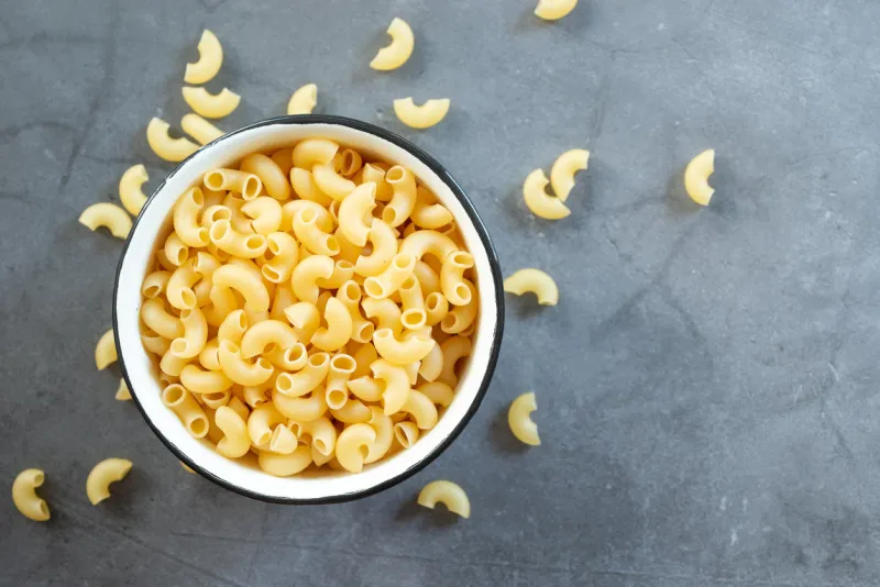 raw elbow macaroni in enamel bowl on dark cement table background