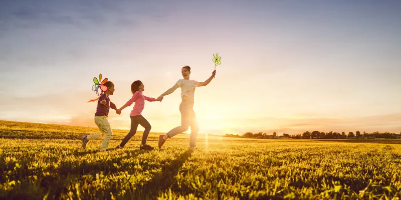 happy loving family is having fun on nature in the summer young mother and two daughters are laughing and playing on meadow at sunset background