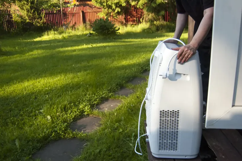 female hands moving a portable air conditioner into a house, outdoor shot