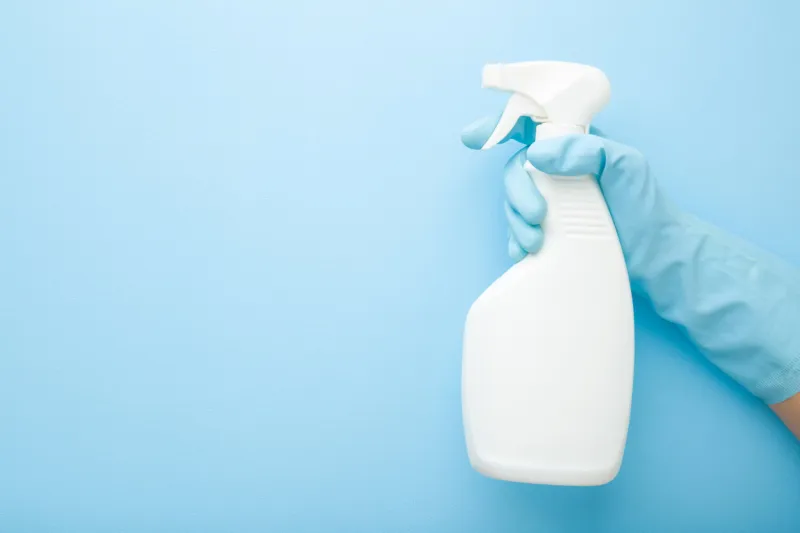hand in rubber protective glove holding white spray bottle detergent for different surfaces in kitchen, bathroom and other rooms closeup empty place for text or logo light pastel blue background