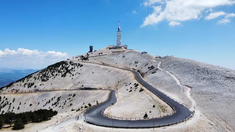 a narrow highway leading to the mont ventoux in france with a blue sky in the background