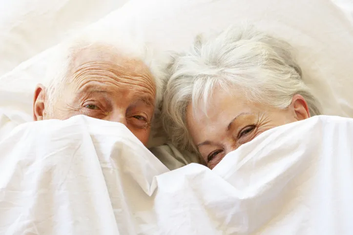 senior couple relaxing in bed hiding under sheets smiling and laughing