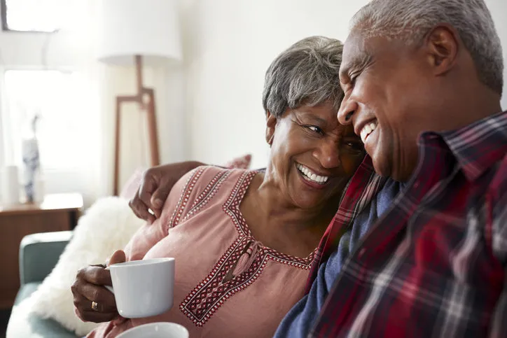loving senior couple sitting on sofa at home relaxing with hot drink