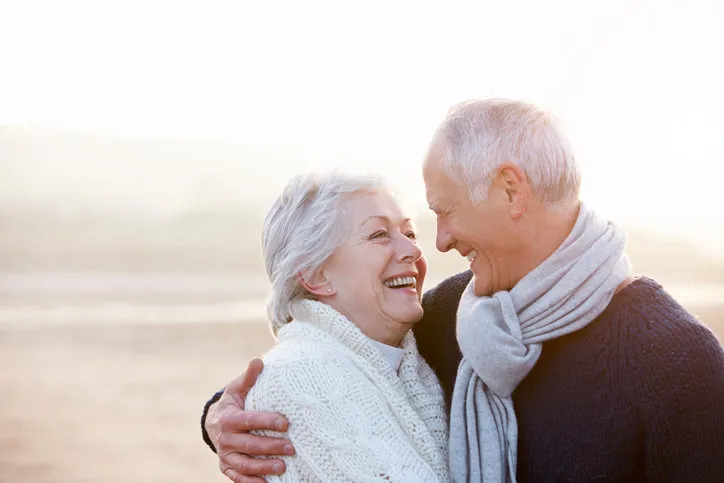 romantic senior couple on winter beach smiling at eachother