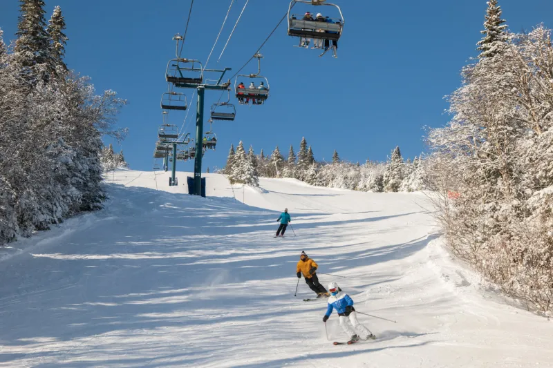 view of skiers climb the ski lift up the hill with snow covered mountains ski chairlift climb above the ski slope