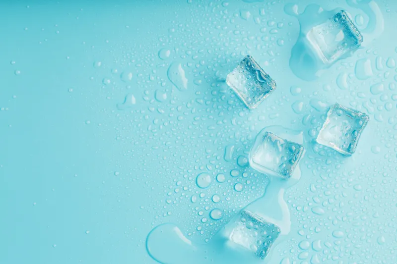 ice cubes with water drops scattered on a blue background, top view refreshing ice