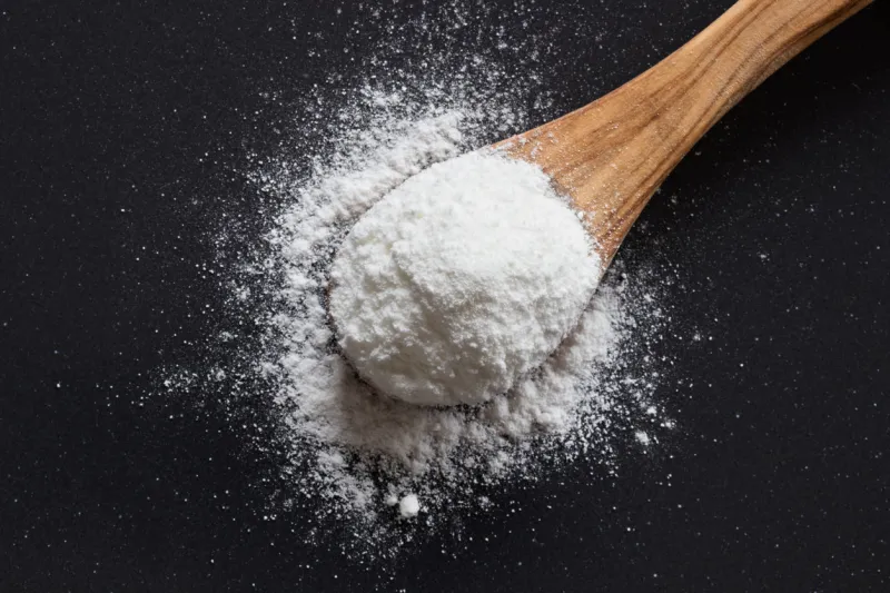 baking soda on a wooden spoon on dark background, top view
