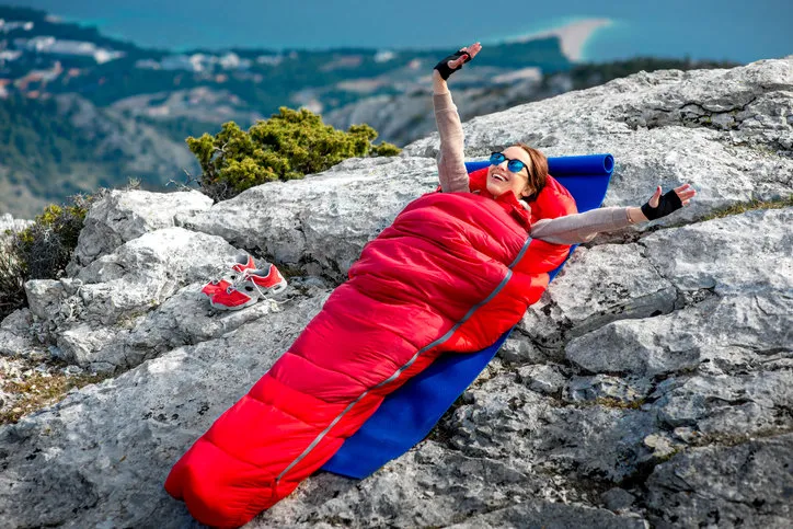 young woman waking up in red sleeping bag on the rocky mountain